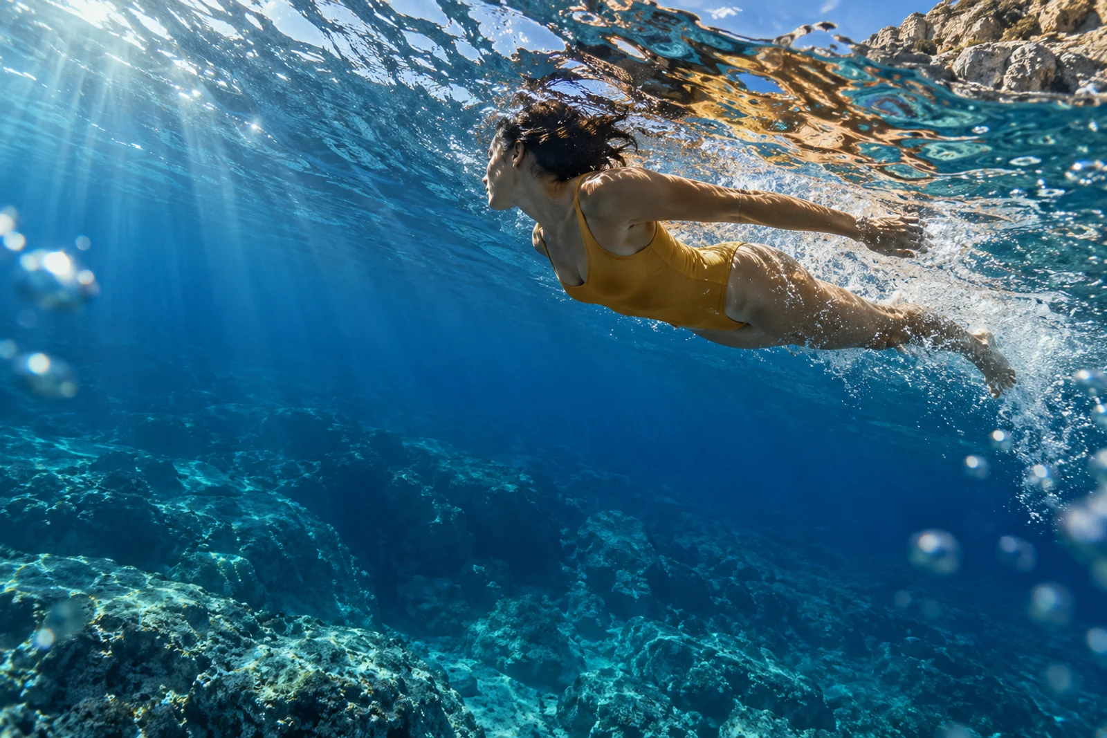 Uma pessoa nadando no mar, vista debaixo da água sob a luz do sol